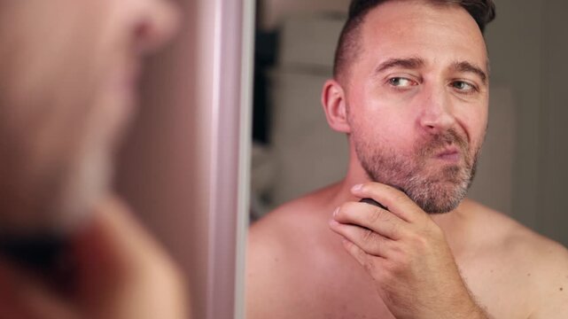 Reflection reveals grooming indecision, Contemplating shave in morning mirror, Man considers trimming beard before starting day, Hesitant man examines jawline in bathroom mirror before grooming