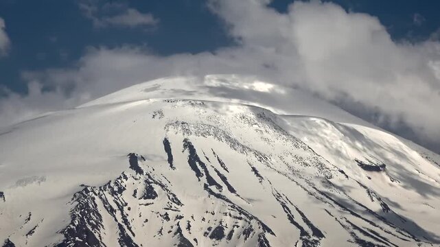 Time lapse clouds swirl around snowy summit of Mount Kilimanjaro, Africa highest peak. Fast motion vapor streams hug ice capped volcano crest, revealing dramatic sky shifts above Tanzania.