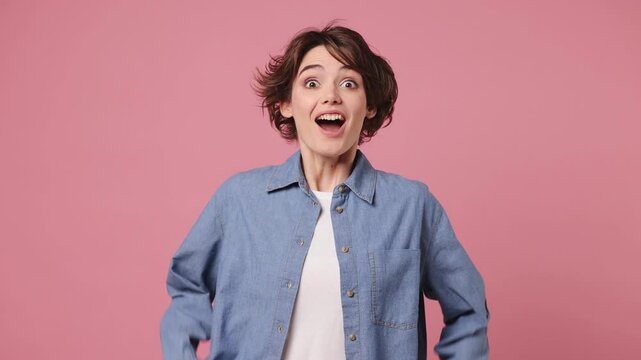 Young woman wears blue shirt white t-shirt casual clothes look camera surprised ask what wow omg no way do winner gesture say yes celebrating put hands on face isolated on plain light pink background