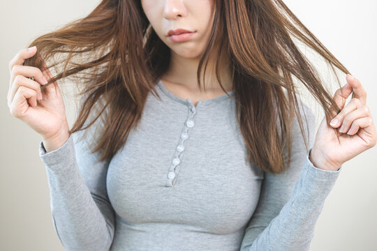 Damaged Hair, frustrated asian young woman, girl hand in holding splitting ends, messy unbrushed dry hair with face upset, long disheveled hair, health care of beauty. Portrait isolated on background
