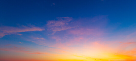 Obraz premium Beautiful sunset sky with orange and blue gradient clouds background,A stunning panoramic view of the twilight sky during sunset, featuring a vibrant gradient of deep blue, purple, and golden orange 