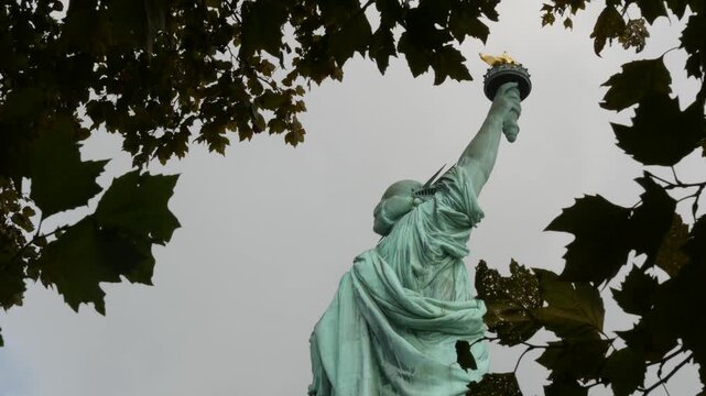 Statue of Liberty on Liberty Island, New York, United States. Cooper monument, symbol of democracy and patriotism near Manhattan, NYC USA. American independence. Autumn fall leaves. From behind, back.