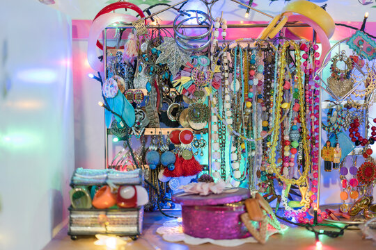 A vibrant collection of colorful necklaces, bracelets, and earrings are displayed on a stand, adorned with festive lights.