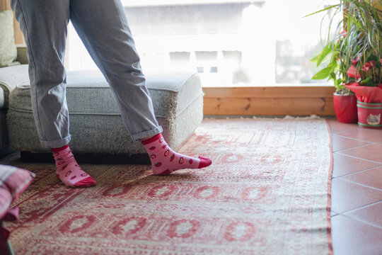 A person wearing light blue jeans and pink strawberry-patterned socks stands near a sofa and a window.