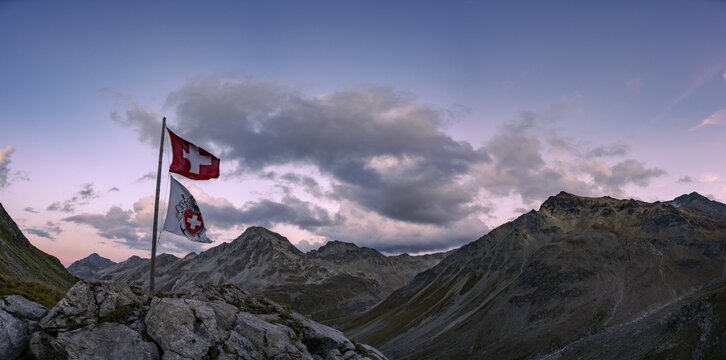 Swiss flag and flag of the SAC with cloudy sky at blue hour and Engadine mountains, St Moritz, Engadine, Grisons, Switzerland