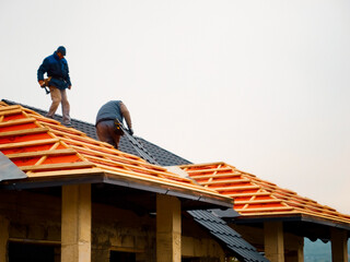 Construction workers are installing metal tiles on a roof using wood and anti-condensation foil. The process takes place on a residential building under construction.