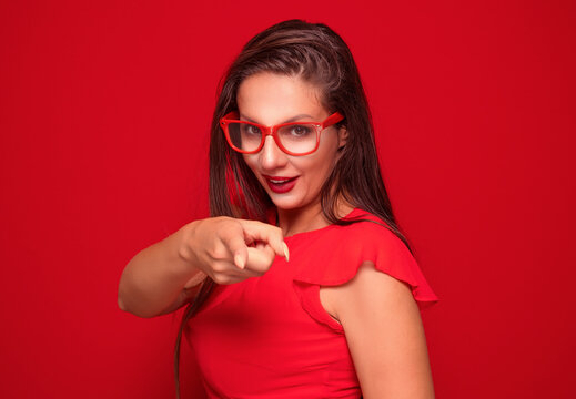 Funny scared woman pointing or showing with finger to something, isolated on red background.