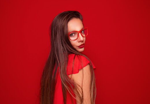 Serious young woman looking at camera, isolated on red background. Front view portrait of a pretty girl.