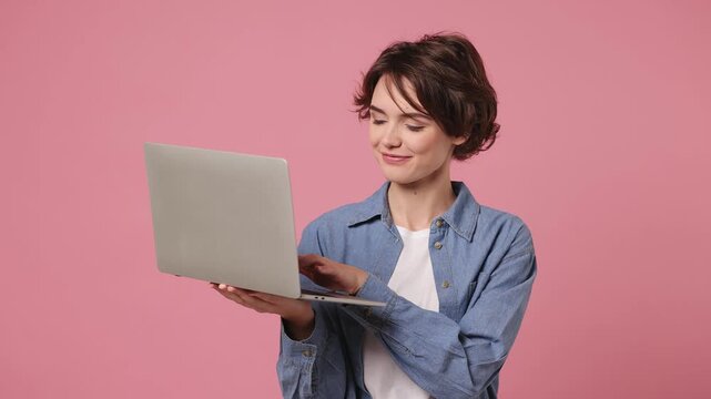 Smart IT user young woman she wears blue shirt white t-shirt casual clothes hold in hand use work typing on laptop pc computer isolated on plain pastel light pink background studio. Lifestyle concept