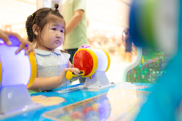 Little Asian girl playing drum arcade game at indoor playground,A cute little East Asian girl...