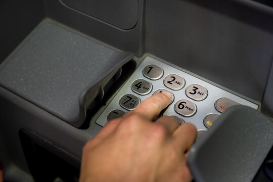 Hand at an ATM, entering the PIN, withdrawing money