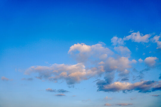 A serene view of white and gray clouds against a blue sky, a dusk or sunset. The sun is low on the horizon, creating a natural backdrop.