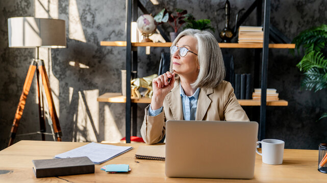 Middle-age woman using laptop computer for business studying, having videocall with online virtual webinar training meeting, writing notes. Focused businesswoman working in office. Copy space
