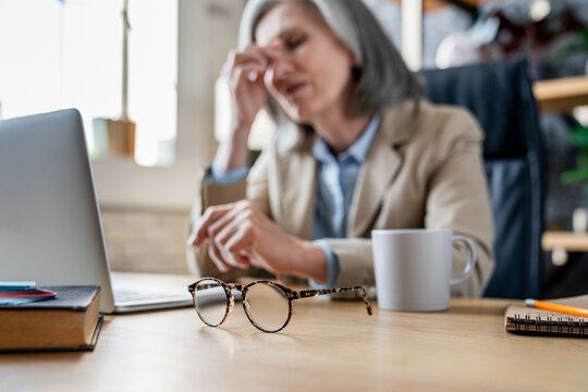Business, woman and headache of eye strain in office for wrong glasses prescription, deadline pressure or burnout. Mature person, tension migraine at desk with brain fog. Focus on eyeglasses