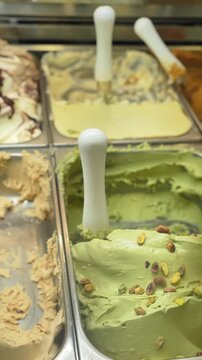 A row of ice cream flavors are displayed in a display case. The flavors include chocolate, vanilla, and green tea