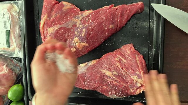 Food Preparation for BBQ &ndash; Hands Adding Salt to Raw Beef for Traditional Asado