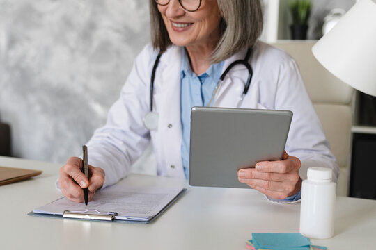 Doctor writing medicine prescription on clipboard and working on desktop computer pc tablet at doctor's office in hospital, treatment plan. Doctor working at office, filling insurance document