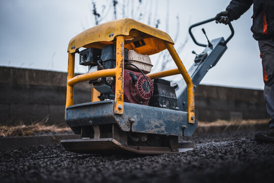 Worker working with a vibrating plate machine. Worker operates machine gravel compactor to compress gravel on construction site