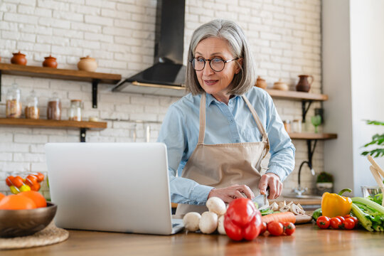 Smart eating. Confident senior woman wife using laptop online app website to find healthy salad recipe search meal idea online in culinary blog when cooking natural vegetable food at home kitchen.