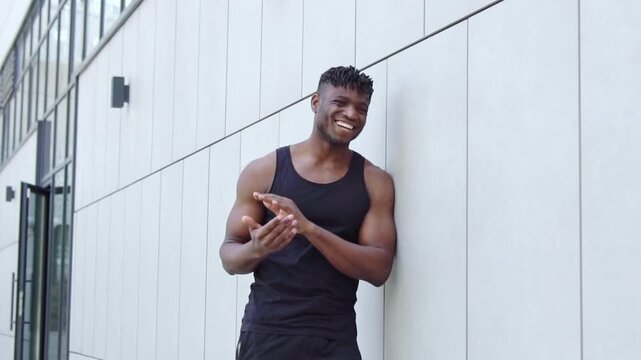 African American man with headphones mocks and laughs while pointing at the camera, sporty guy accuses and ridicules you on city street