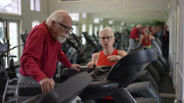 Senior man exercises on a machine with support from his trainer at the gym, focusing on his fitness and health goals.