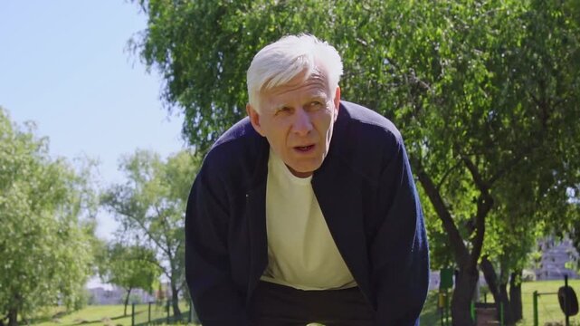tired elderly man is exercising in the park and is starting to catch his breath, exhausted gray-haired pensioner is suffering from the heat after running outdoors