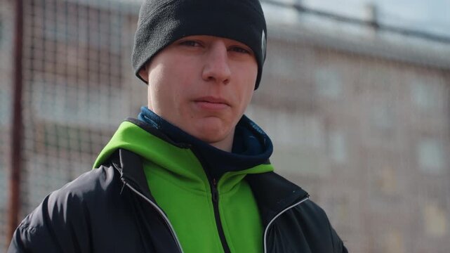athlete ponders silently, reflective sportsman against city skyline, young athlete contemplates after workout near cityscape, quiet athlete pauses on enclosed court with urban background