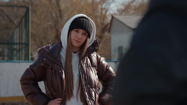 caucasian teen coach stands by goal with hands on hips, assertive posture and watchful expression, winter jacket layered over hoodie, urban neighborhood court setting, leadership and friendly