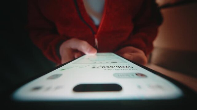 Close-up wide angle male hand holding smartphone. Man walks using phone at home. Financial app showing portfolio growth and rising chart. Camera locked at device screen, motion background