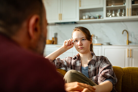 Teen girl talking with parent on sofa at home kitchen