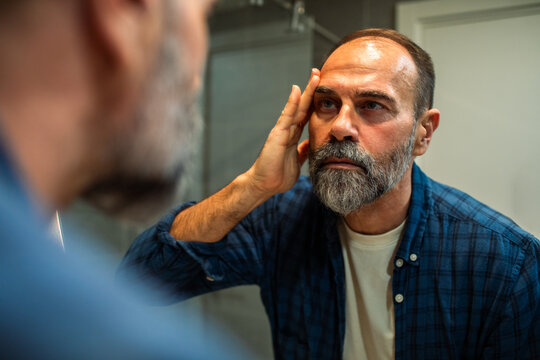 Middle-aged man examining face in bathroom mirror