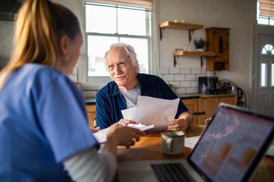 Home care nurse assists senior man at kitchen table