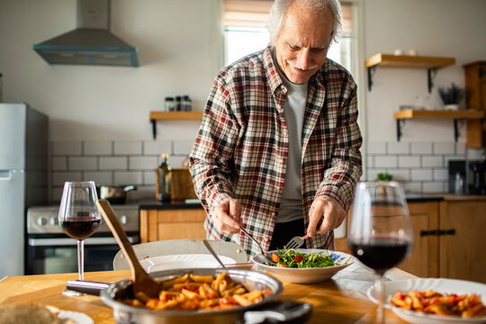 Senior man serving salad in home kitchen