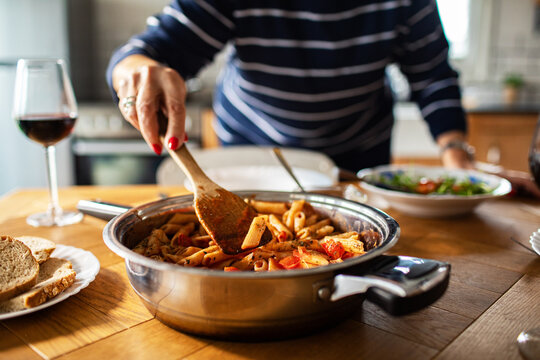 Home cook stirring penne pasta on dining table