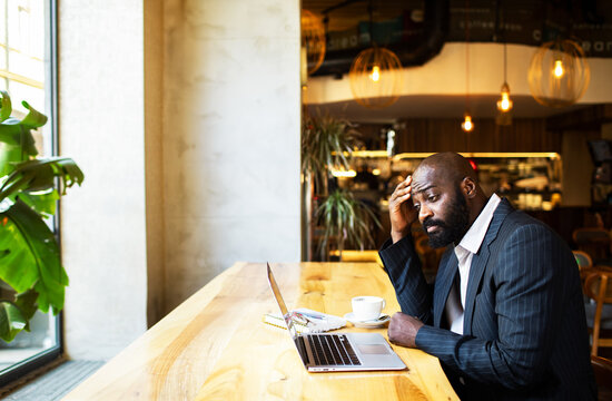 Stressed businessman working on laptop at cafe counter