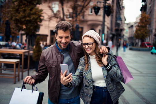 Smiling couple taking selfie while shopping in city street