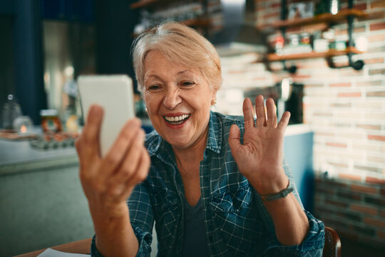 Happy senior woman waving during video call in home kitchen