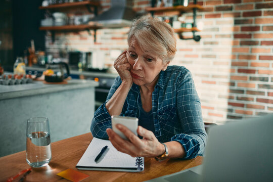 Senior woman frustrated with smartphone at home kitchen table