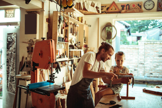 Carpenter teaching child woodworking in home workshop