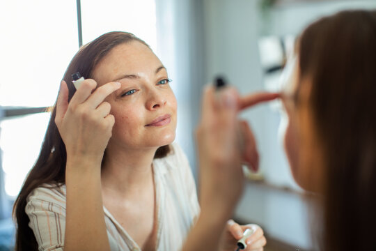 Young woman applying eye cream in front of home mirror