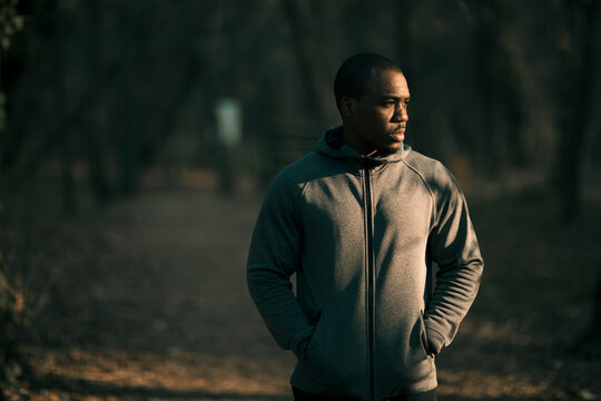 Man in hoodie standing on forest trail at dusk