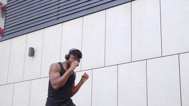 African American man in sportswear boxing outdoors with headphones, athletic guy practicing punches and doing shadow boxing on urban background
