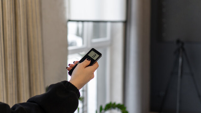 a woman holds in her hand a remote control for an automatic roller shutter control system. raising and lowering of blinds, electronics, technologies, automation, home coziness and comfort
