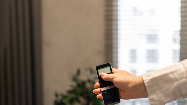 a woman holds in her hand a remote control for an automatic roller shutter control system. raising and lowering of blinds, electronics, technologies, automation, home coziness and comfort