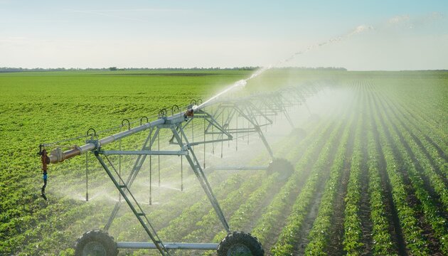 Aerial view of center pivot irrigation system watering crops in a vast agricultural field on a sunny day