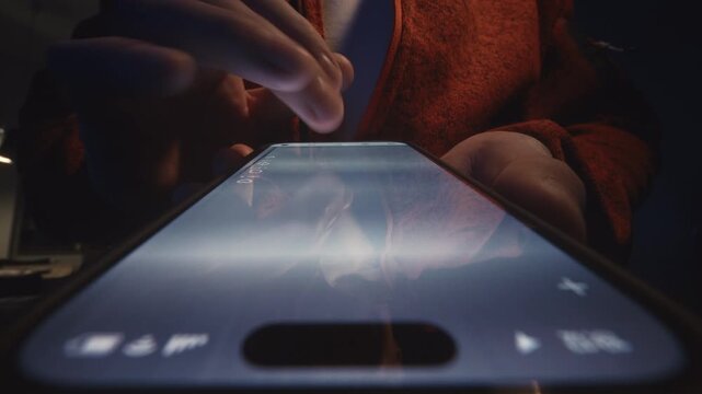 Extreme close-up male finger scrolling smartphone screen in deep darkness at night. Swiping finger, motion blur on phone screen. Evening online browsing, digital content consumption