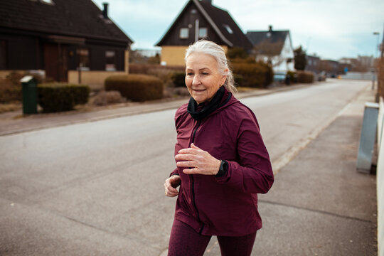 Active senior woman jogging on suburban street in cool weather