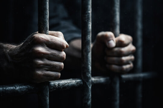 Close-up of human hands gripping prison bars in a dark, confined space