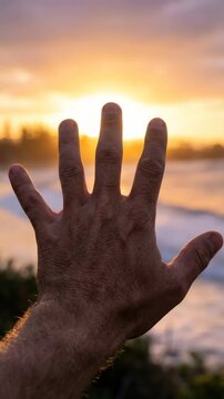 Hand gestures against sunset at beach. Person shows five fingers while enjoying warm evening light. Relaxing atmosphere captured in vertical format. Perfect for travel and lifestyle projects.