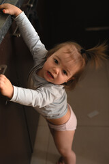 Fototapeta premium curious toddler reaching and leaning on a dark kitchen cabinet countertop in soft warm light, candid domestic portrait highlighting skin tones, muted browns and pinks, playful intimate expression